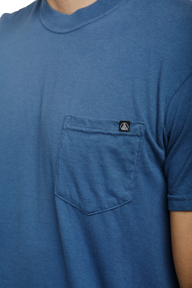The person is wearing the Heavyweight Midnight Pocket Tee, crafted from garment-dyed cotton. It features a front pocket on the left side with a small logo tag above it, capturing the essence of midnight pocket tees perfectly.