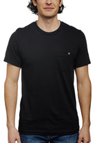 A man stands against a white background wearing the Black Pocket Tee w/ SFP Clip Label, crafted from Airlume cotton, epitomizing the basics line.