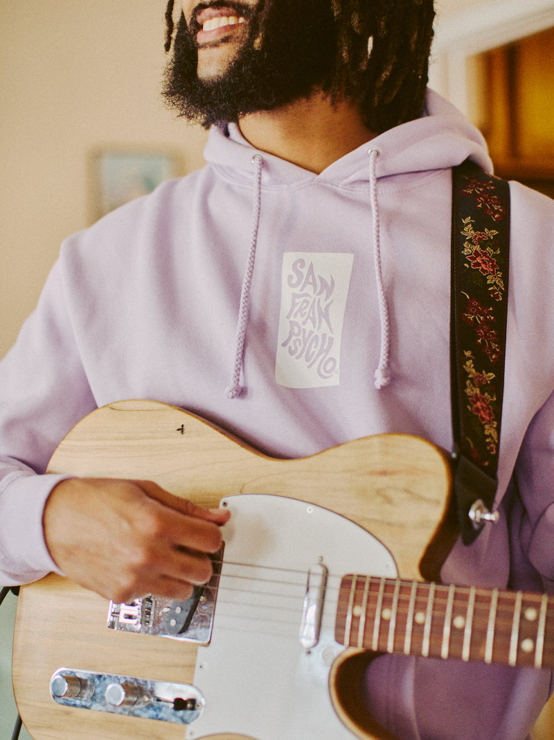 A person in a Trippy Psycho Pullover Hoodie from the Spring 2023 Collection strums a guitar adorned with a floral strap.