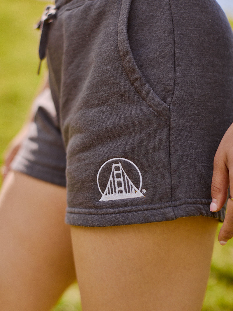 A woman is relishing the sunny outdoors, dressed in the Women's Embroidered Logo Jogger Shorts made from a gray cotton/polyester blend, ideal for casual outings.