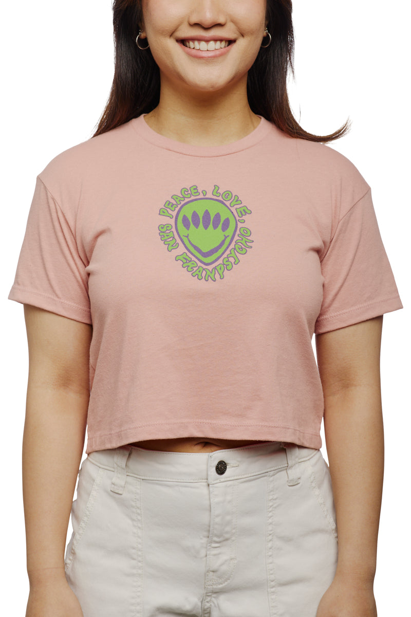 Woman wearing a pink Peace Love Alien Crop Top featuring a green paw print design.
