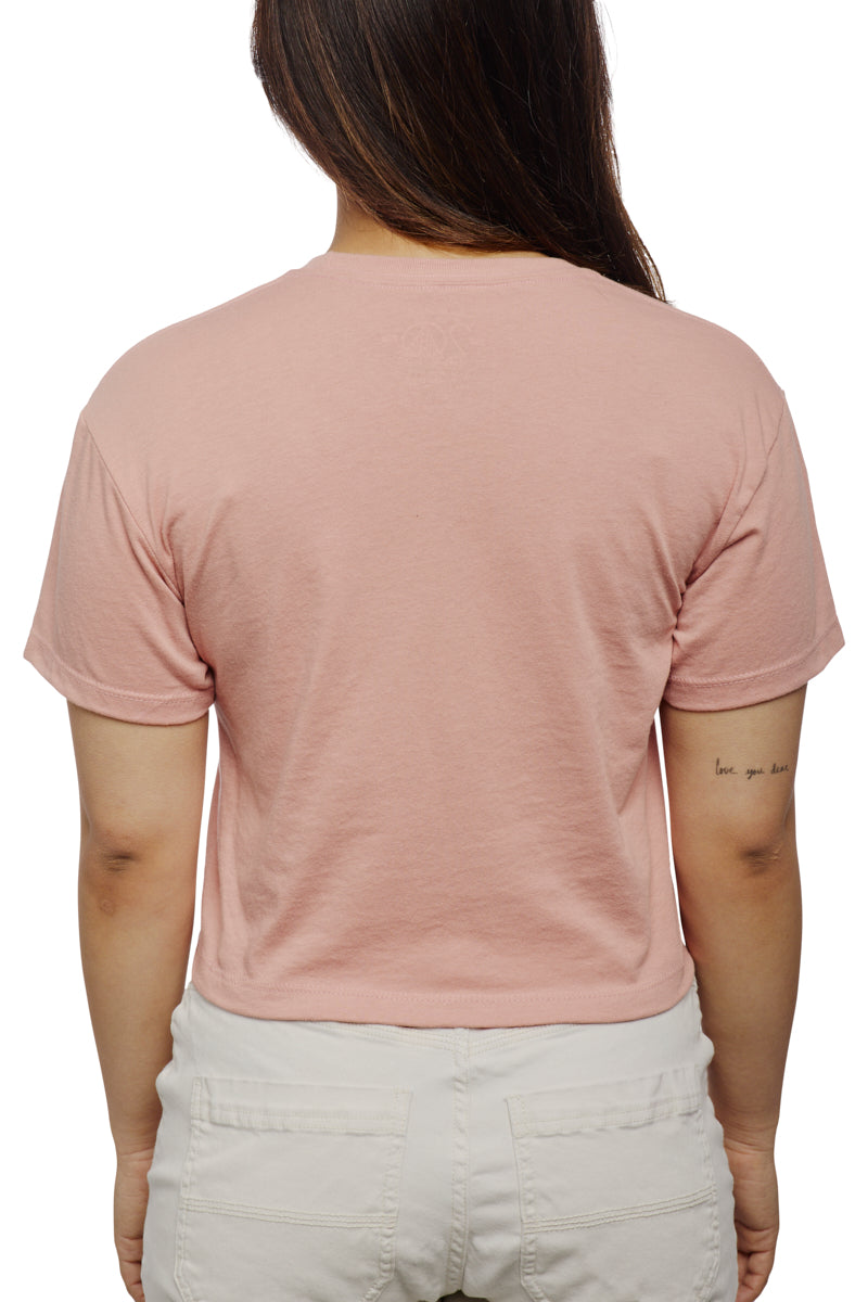 Back view of a person wearing a Peace Love Alien Crop Top and white pants, showcasing a tattoo on their right forearm.