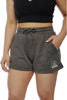 A person wearing Women's Embroidered Logo Jogger Shorts in gray, featuring a cotton/polyester blend and a black crop top, stands casually with one hand in their pocket.