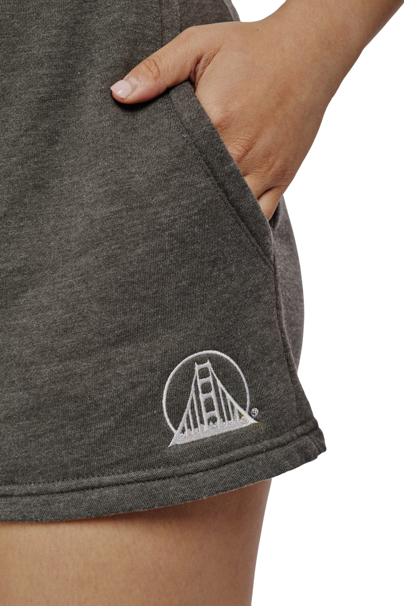 Close-up of a person wearing Women's Embroidered Logo Jogger Shorts made from a cotton/polyester blend, showcasing an embroidered Golden Gate Bridge logo, with their hand casually tucked in the pocket.
