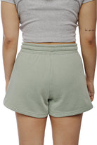 A person wearing a gray shirt and Women's Embroidered Logo Jogger Shorts in green, crafted from a cozy cotton/polyester blend, showcases a tattoo on their left arm.
