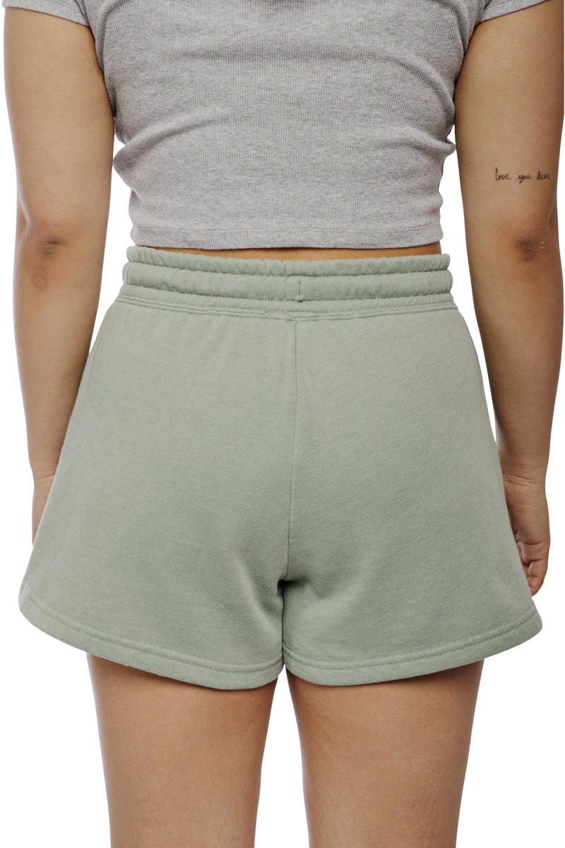 A person wearing a gray shirt and Women's Embroidered Logo Jogger Shorts in green, crafted from a cozy cotton/polyester blend, showcases a tattoo on their left arm.