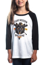 A girl wearing the Youth Take Meeeow Baseball Tee, which features a cat graphic and the text "TAKE MEEOW THE BALL GAME" in black and white—ideal for baseball season. Available in kids' sizes.