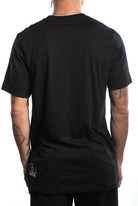 Wearing the Build Bridges Not Walls Tee in black, a person shows off their tattooed arms with the subtle hand-printed phrase on display as they face away from the camera.