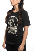 A person wearing the "Build Bridges Not Walls Tee," a black shirt featuring a hand-printed bridge graphic and the text.