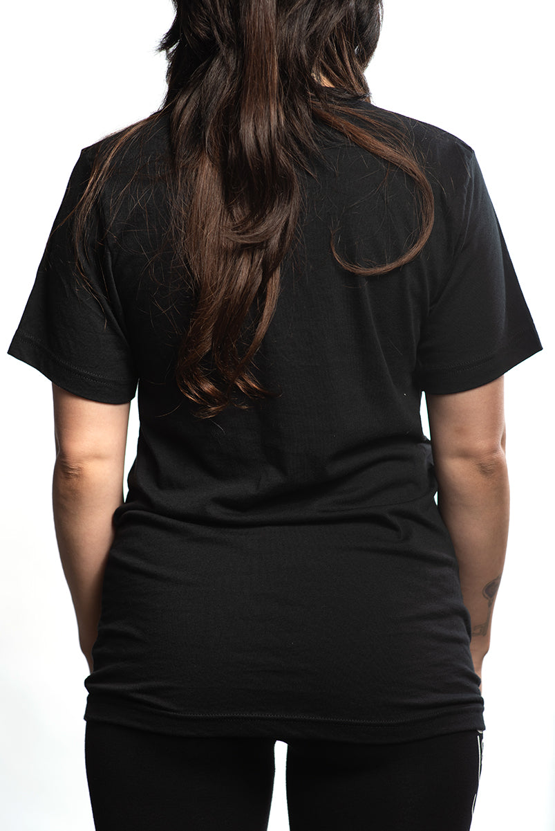 A person with long hair is wearing a hand-printed Build Bridges Not Walls Tee in black, viewed from the back.