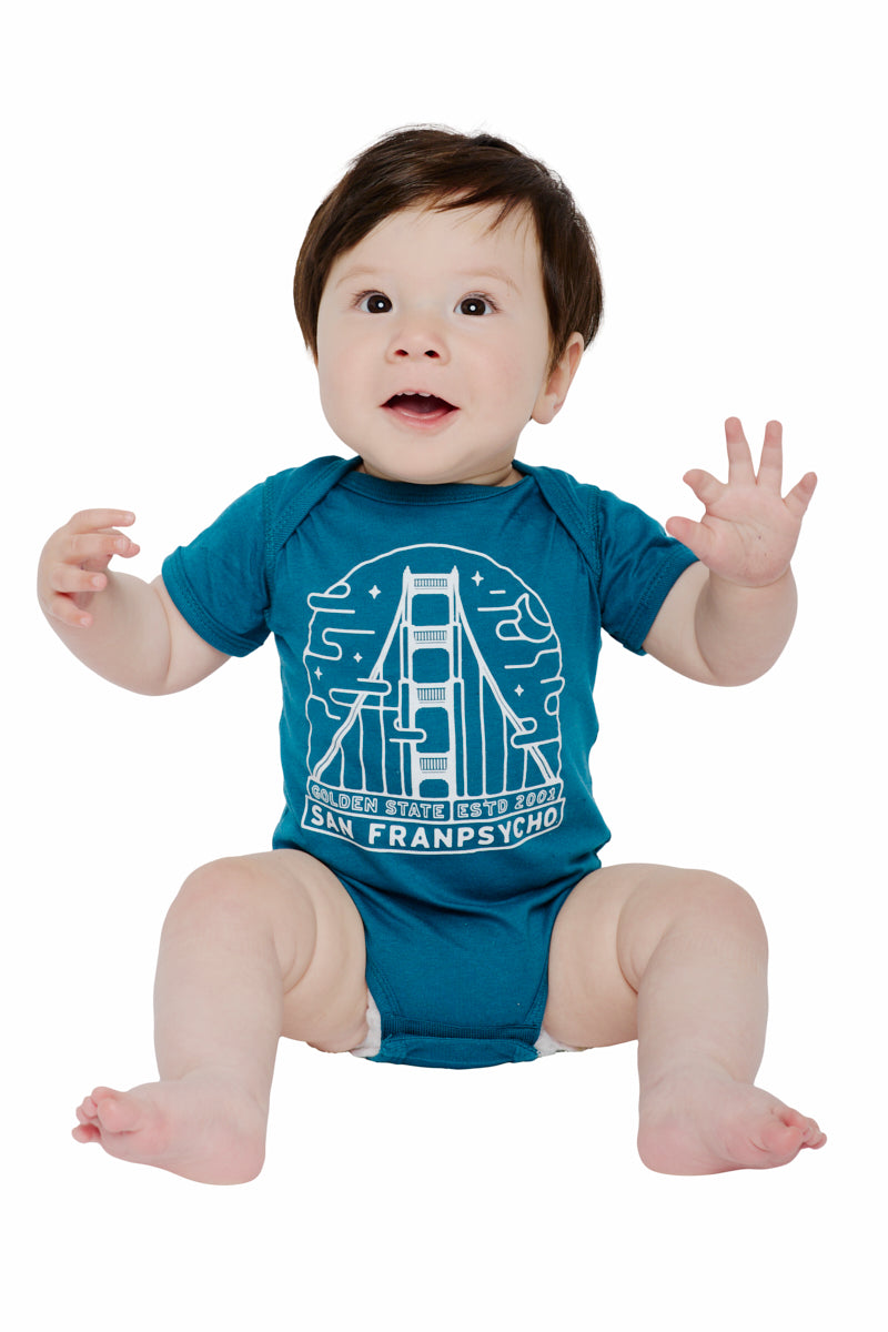 A baby sitting, dressed in the Teal Fogtown Onesie made of 100% cotton, features a bridge graphic with "Golden State" and "San Franpsycho" in a charming design.