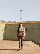 Sporting the Desert Daze Crewneck from the unisex Summer 2023 collection, a woman in sunglasses confidently walks on a concrete surface, set against a backdrop of clear blue skies.