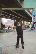 Wearing a Banned in SF Tee, a person with dreadlocks skates smoothly through the graffiti-laden San Francisco skate park, epitomizing Fall Punk Rock 2023.