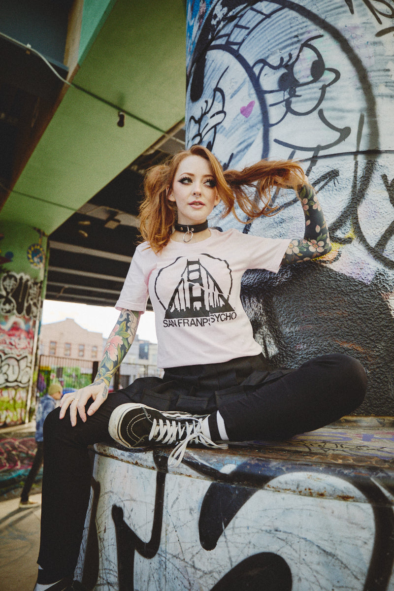 A person with tattoos poses playfully in a vibrant graffiti-filled space, flaunting the Shredder Logo Tee that embodies the essence of Punk Rock 2023.