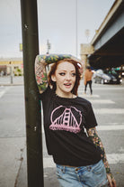 A woman wearing a Women’s Black & Pink Logo Tee featuring a vintage San Franpsycho Golden Gate Bridge graphic.