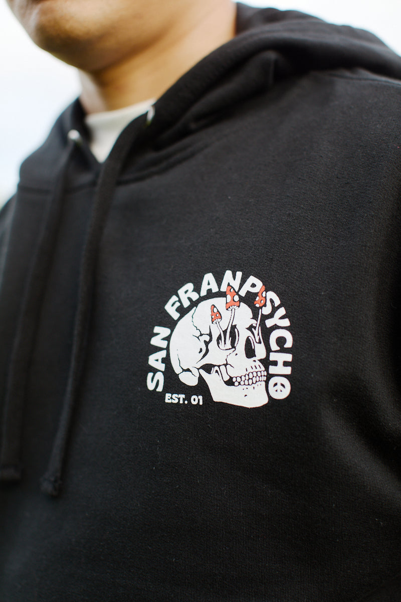 Close-up of a person wearing the Shroom Skull Pullover Hoodie in black, made from 100% cotton and featuring the Shroom Skull design along with the San Franpsycho Est. 01 logo.