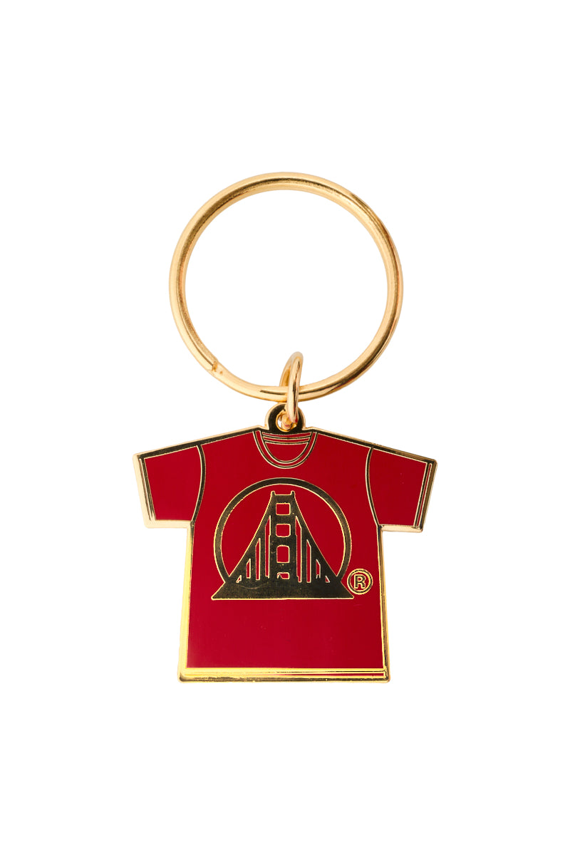 Gold Logo Tee Keychain with a red shirt-shaped pendant, featuring a black enamel stylized tower design.