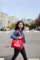 A woman strolls down the city street, her denim jacket complementing the Heart Logo Tote slung over her shoulder, expertly hand-printed on 100% canvas.