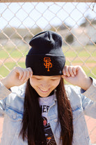 Person smiling, adjusting the Psychos Logo Beanie, proudly standing in front of a chain-link fence.