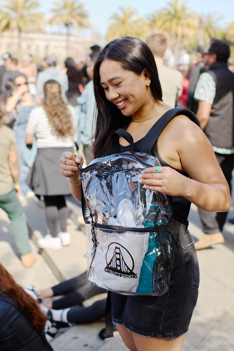 A woman smiles as she enjoys the sunny day at the festival, wearing a clear backpack featuring the SFP logo.