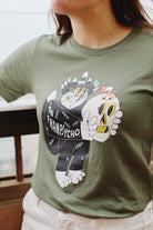 A person wearing the striking green Battle Cat Tee, a unisex shirt featuring an imaginative design of a Battle Cat and skull by Ferris Plock.