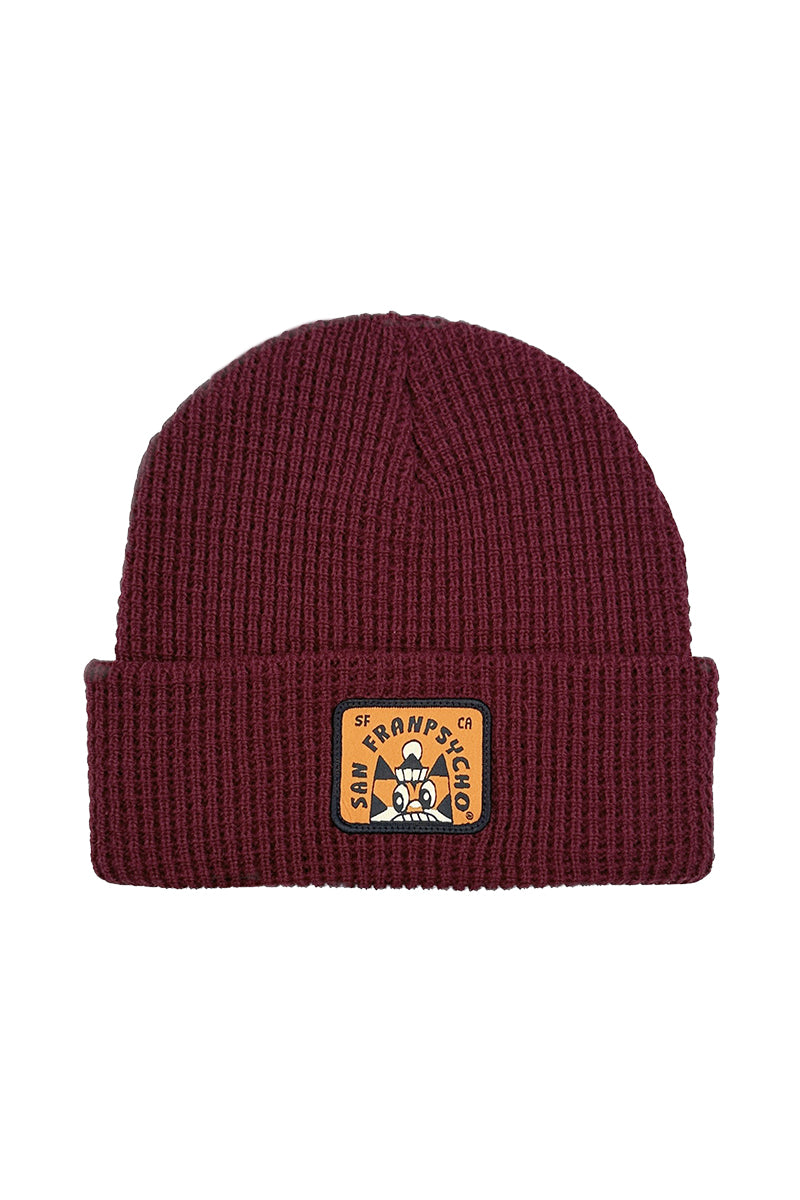 The Cat Stamp Burgundy Waffle Beanie highlights a brown rectangular logo patch on its folded brim, displaying the Cat Stamp design from the Ferris Plock collaboration.