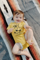 toddler lying on blanket wearing yellow Kitty Poof Onesie
