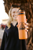 Holding the orange SFP Water Bottle, featuring a San Francisco bridge design, your drink stays perfectly hot or cold with its double-wall vacuum insulation. Its leak-resistant, stylish, and practical for any adventure.