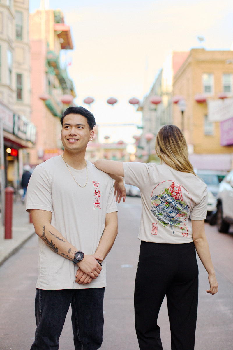 Two individuals wearing matching Year of the Snake Tees, made from soft Airlume cotton and designed for a unisex fit, stand on a lantern-decorated city street.