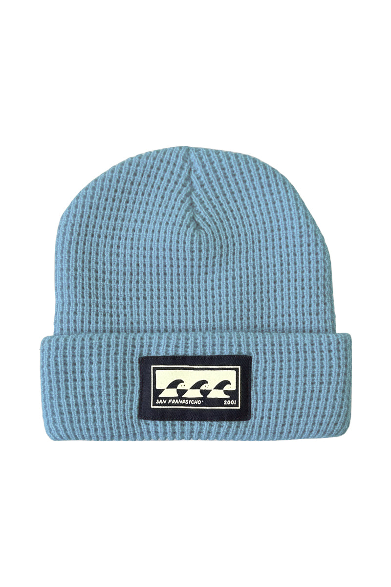 Meet the Blue Waffle Beanie w/ Carved Waves Logo, a light blue knit beanie featuring a folded brim and a black patch with a white wave design in the center. Its the softest beanie for any chilly day, offering unparalleled comfort.