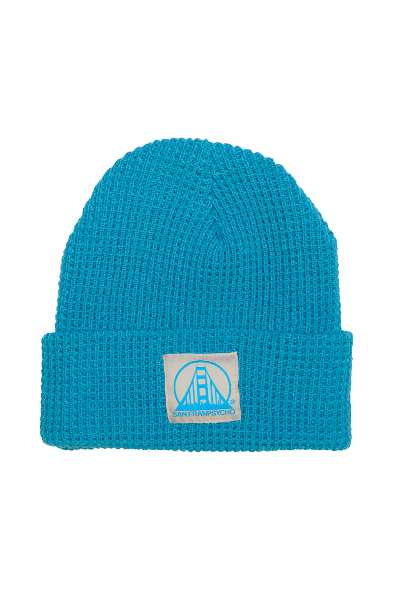 The Cyan Waffle Beanie is a cozy acrylic hat featuring a natural and blue logo patch with San Franpsycho text and a bridge design.