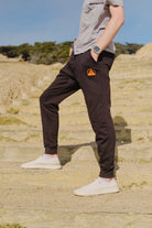 Person in a gray shirt and Black & Orange Embroidered Logo Joggers stands on stone steps outdoors, hands in pockets.