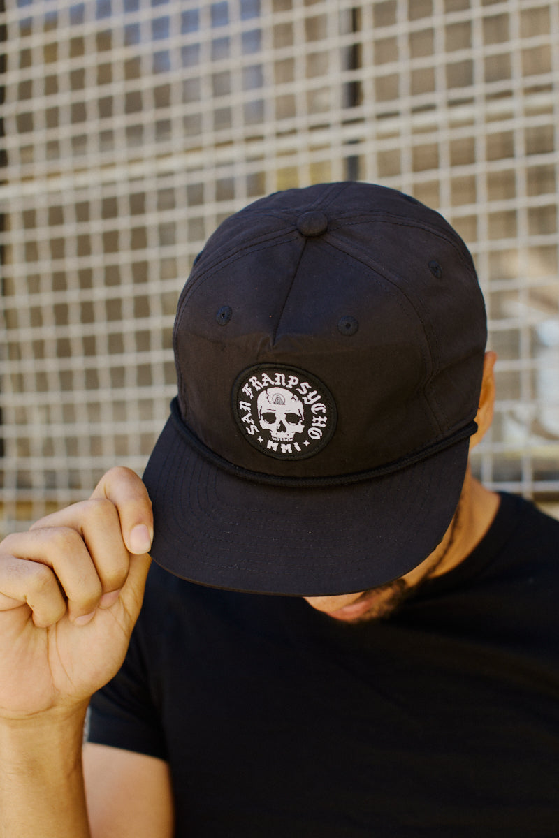 Man in a black shirt tilting a Punk Skull Hat, standing in front of a wire fence.