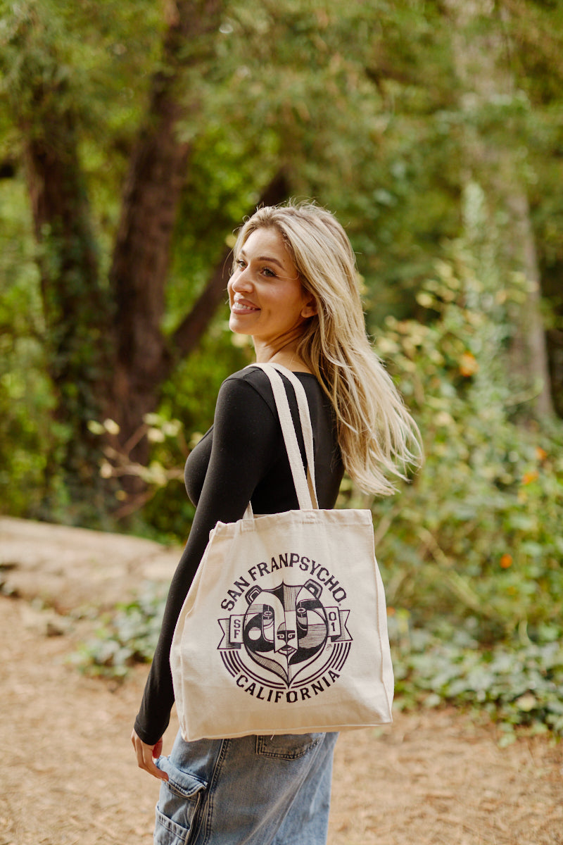 A woman outdoors smiles while carrying the Bear Essentials Tote, a San Franpsycho California canvas bag featuring a graphic logo.