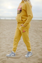 A person in a yellow hoodie and Kelly's Cove Joggers walks on the beach, wearing gray Nike sneakers.