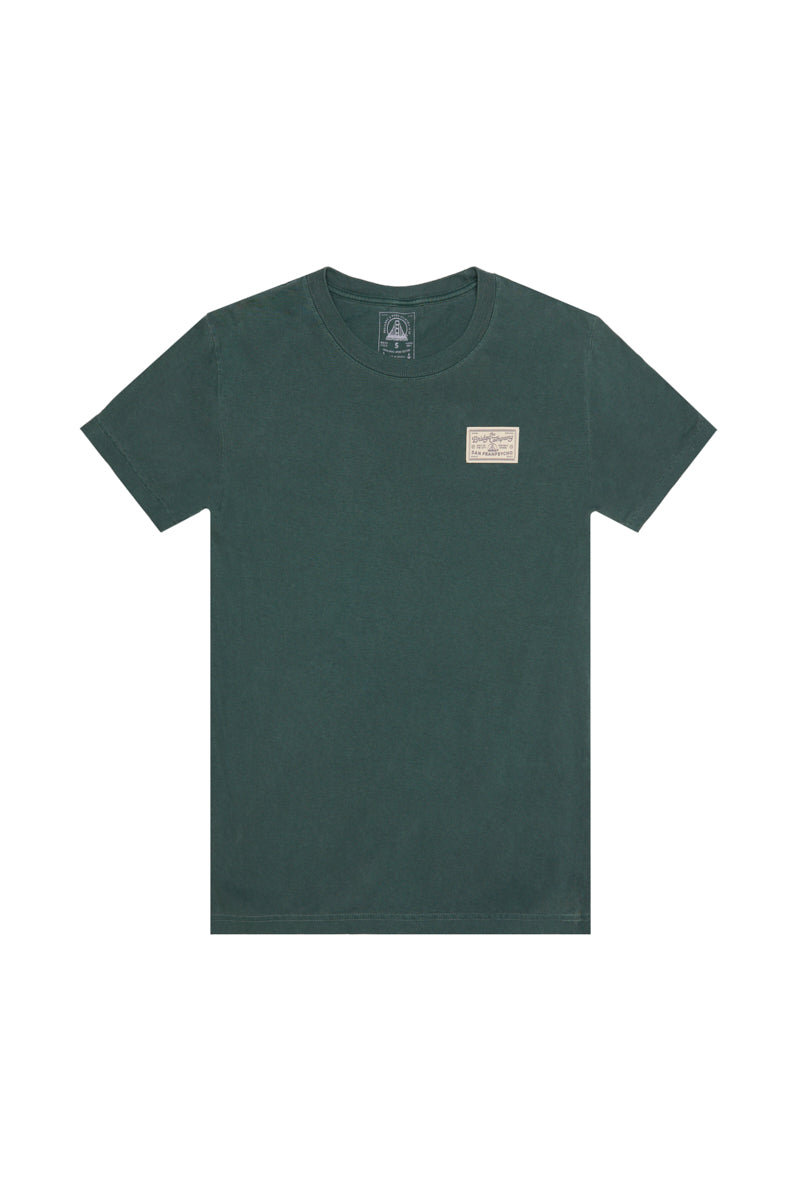 The Bridge Co Tee is a dark green heavyweight cotton shirt with a small rectangular logo patch on the left chest, ideal for a workwear-inspired style.