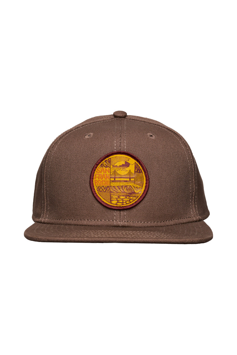 The Elemental Hat is a brown flat-brim cap with an unstructured crown and a circular yellow and red nature-themed patch on the front.