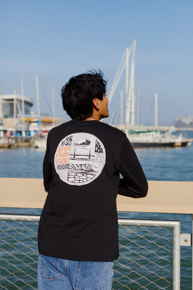 Wearing an Elemental Long Sleeve, a person leans on a waterfront railing with boats and a marina in the background.