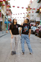 Two people wear Year of the Horse Tees, made from soft Airlume cotton, while standing on a street decorated with red lanterns for Lunar New Year in Chinatown.