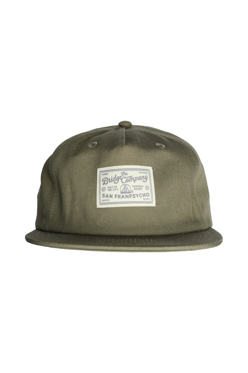 The Bridge Co. Patched Hat is an olive green baseball cap with a flat brim, featuring a white San Franpsycho patch on the front and an adjustable back for a one size fits most fit.
