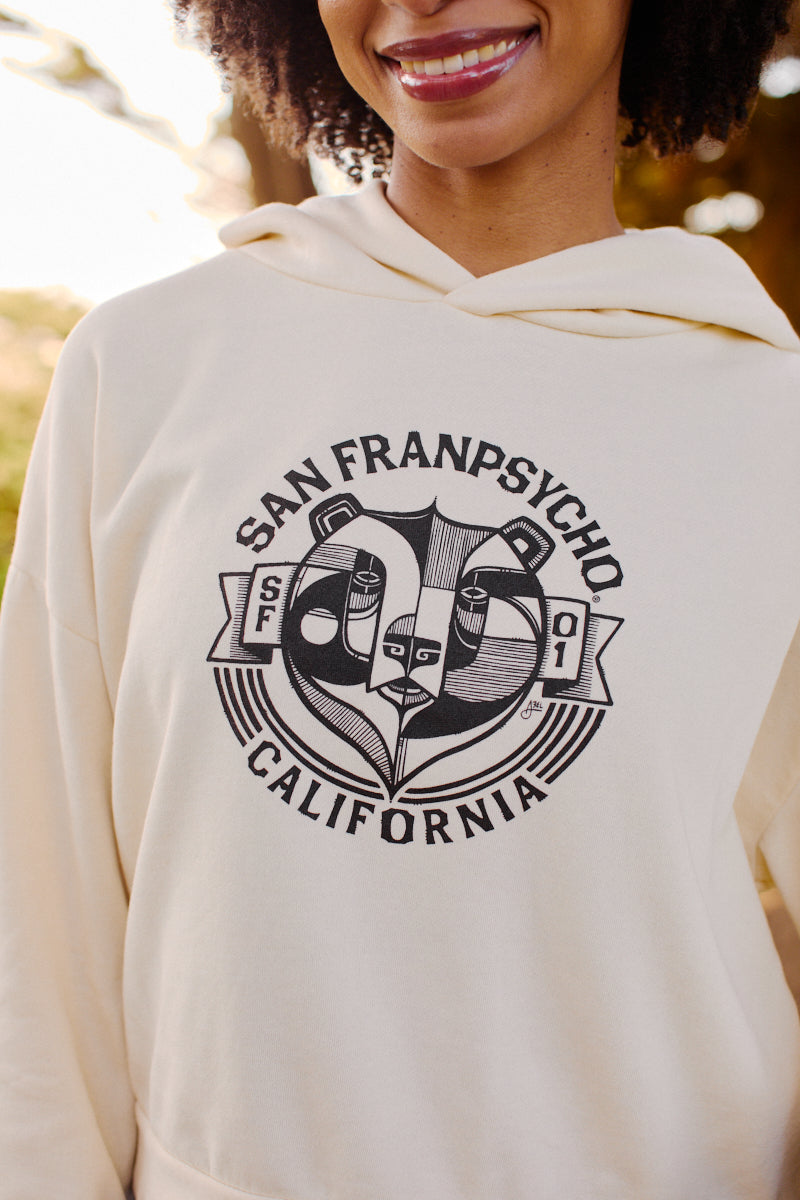A smiling woman wears the Women's Bear Essentials Pullover, an ultra-soft cream hoodie featuring “San Franpsycho California” and a panda logo.