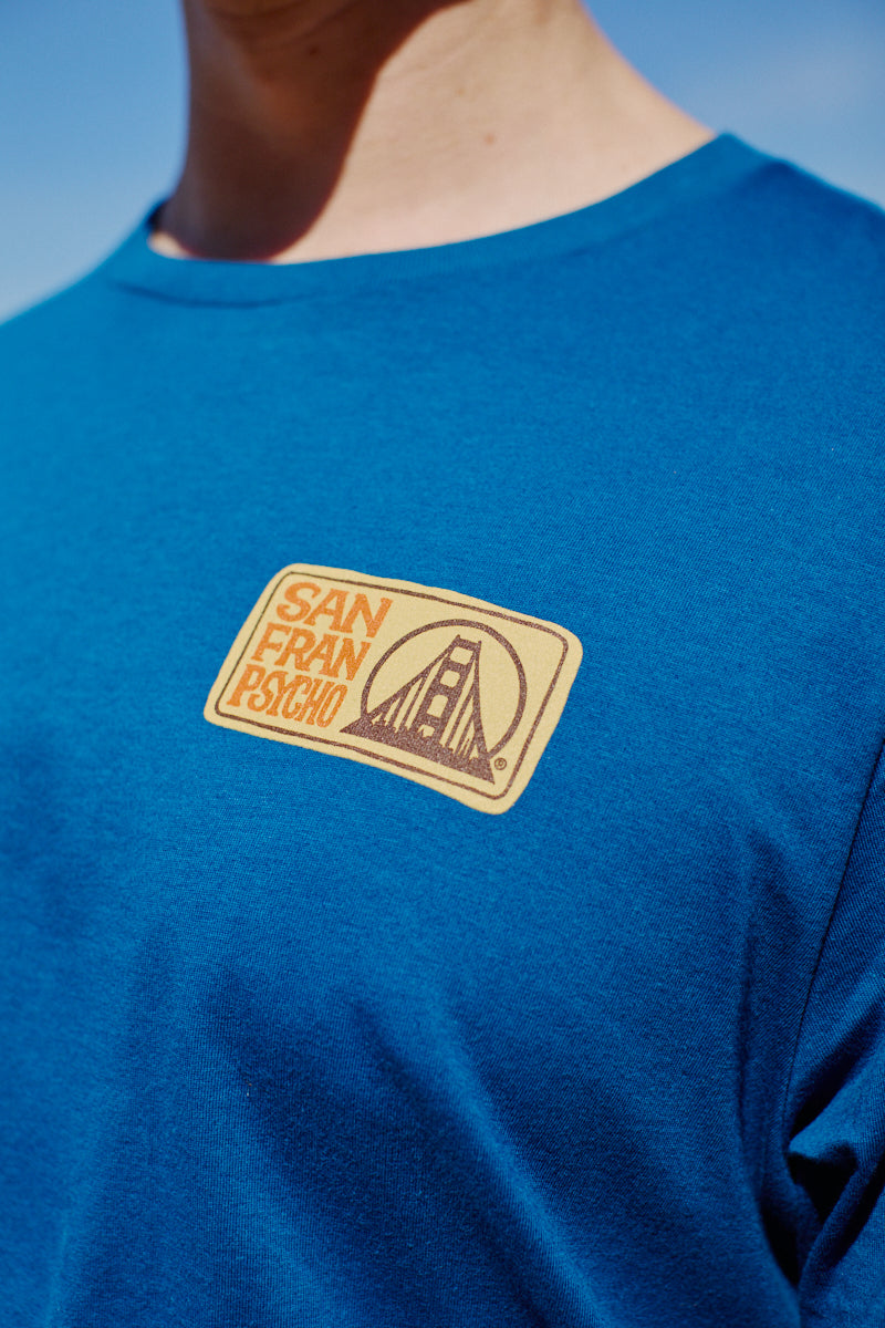 Wearing the Elemental Tee - Blue, featuring a San Franpsycho patch and a Golden Gate Bridge graphic on the chest, captures the spirit of San Francisco.