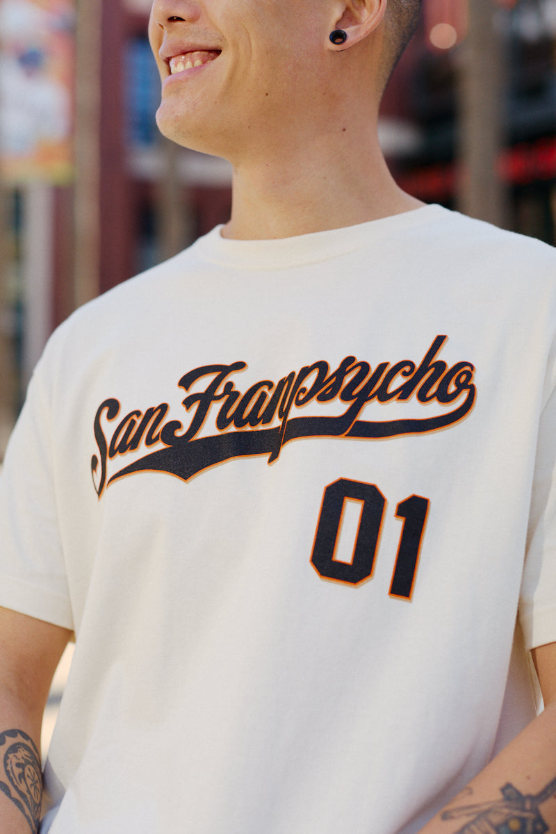 Person smiling, wearing a hand-printed Psychos Script Tee - Natural by San Franspycho 01, with black and orange details that pop and visible arm tattoos.