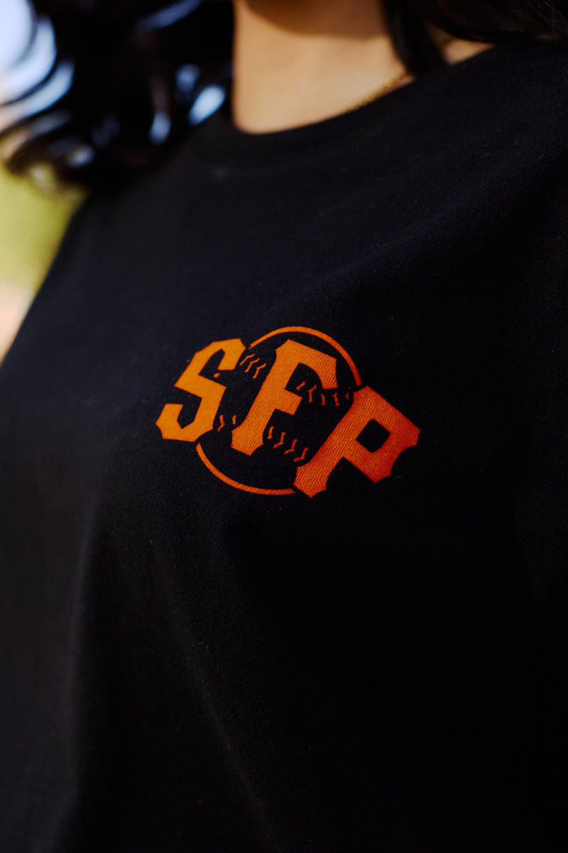 Close-up of the Black & Orange Psychos Tee—a black shirt featuring bold black and orange accents, the SCP logo, and a baseball graphic in the background.