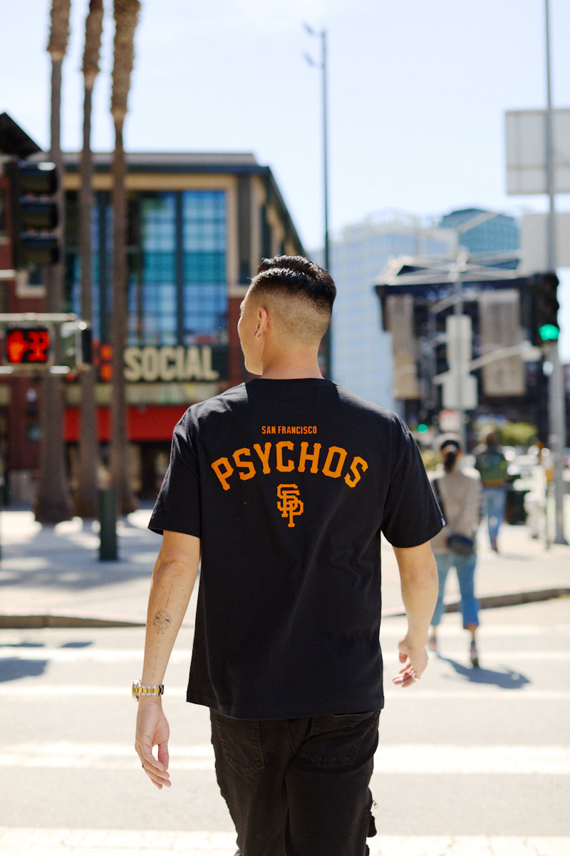 A man crosses a city street sporting the Black & Orange Psychos Tee, showing off his black and orange pride.