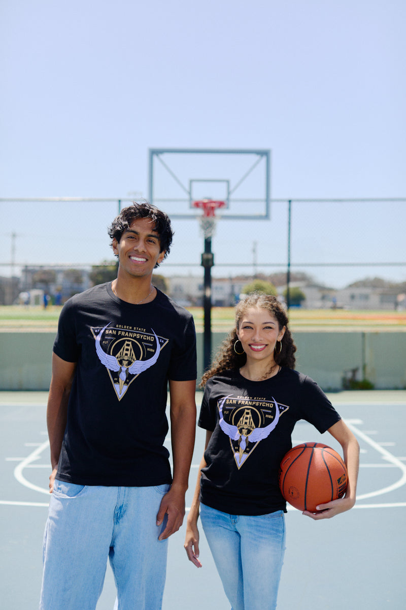 Two people smile on a basketball court in matching black Valhalla Tees, crafted from soft Airlume cotton; one holds a basketball, excited for the Valkyries season.