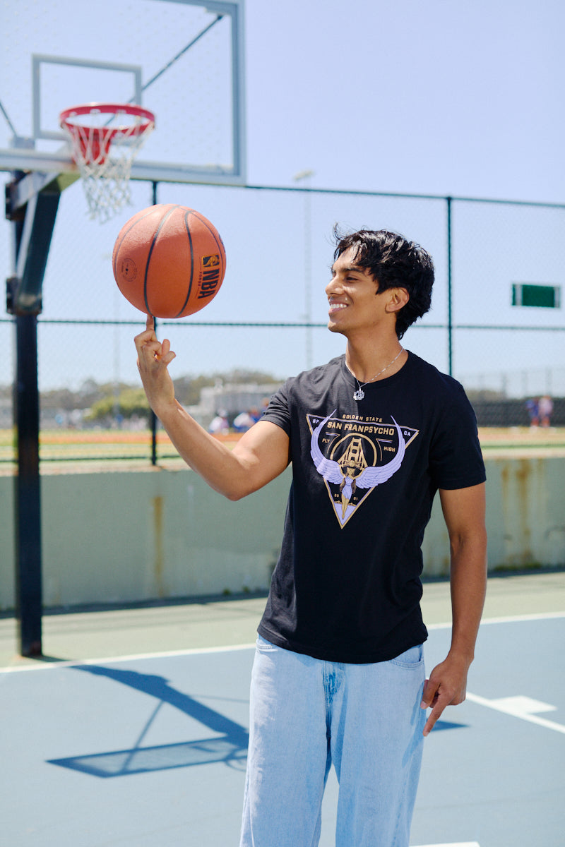 Smiling on an outdoor basketball court, a man wearing a Valhalla Tee spins a basketball on his finger.