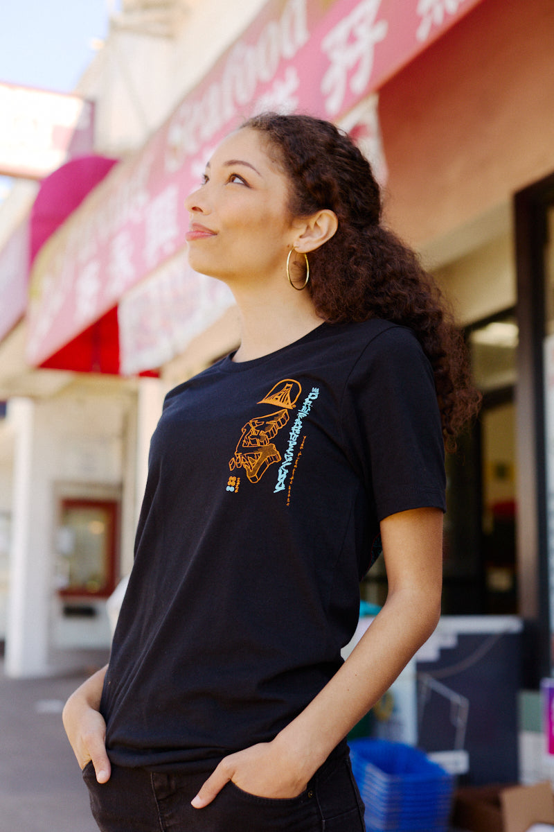 Wearing a Year of the Horse Tee, a woman stands outside among shops and festive signs, embracing the spirit of Lunar New Year.