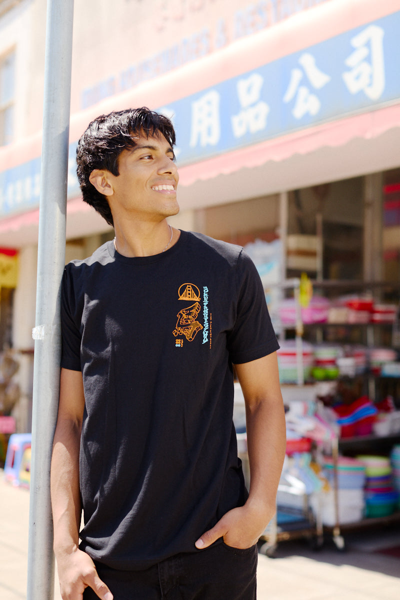 A smiling young man wearing the Year of the Horse Tee stands outside a store with colorful items and Chinese signage, celebrating Lunar New Year.