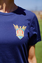 Wearing the WC x SFP Tee—a navy shirt featuring a vibrant, winged crest on the chest—soak up the sun and show off your Team USA pride outdoors.